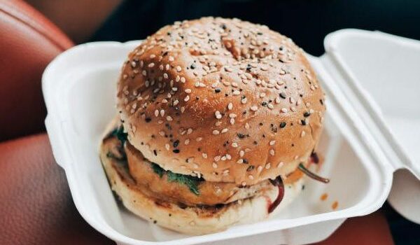 A sesame seed burger in a white takeout container.