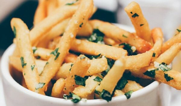 A bowl of seasoned French fries garnished with herbs.