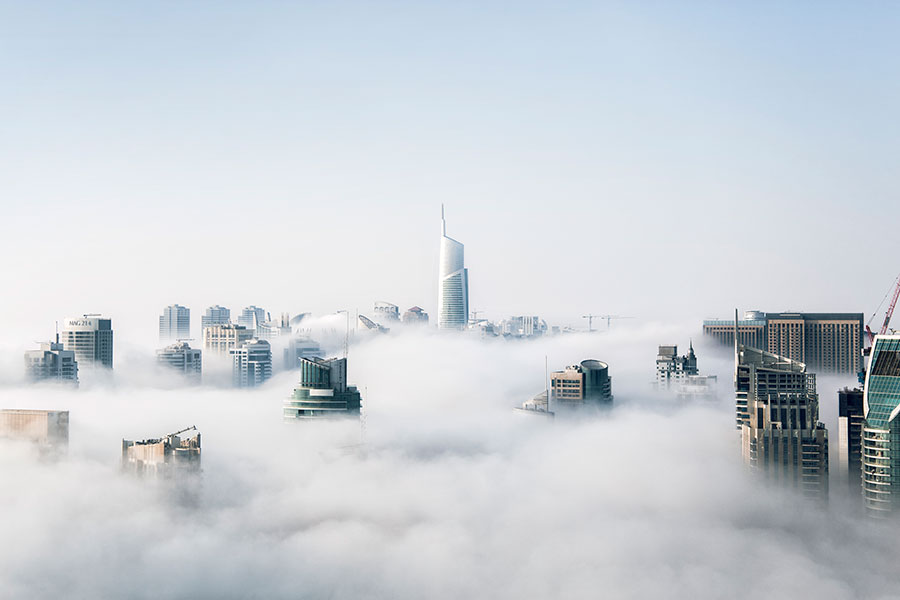 City skyscrapers emerging through dense fog under a clear sky.